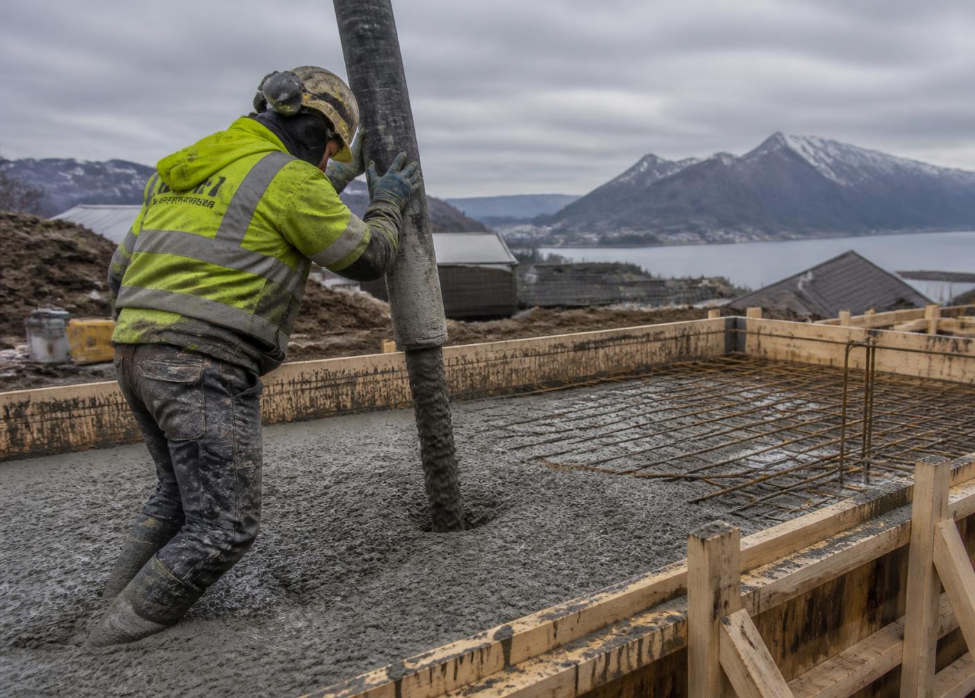 Arbeidar i verneutstyr som styrer betongpumpeslange under støyping av plate